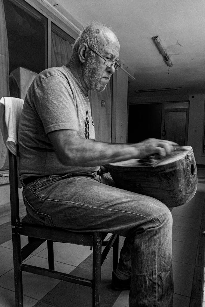 about-us Senior craftsman masterfully honing a traditional drum in black and white indoor setting.